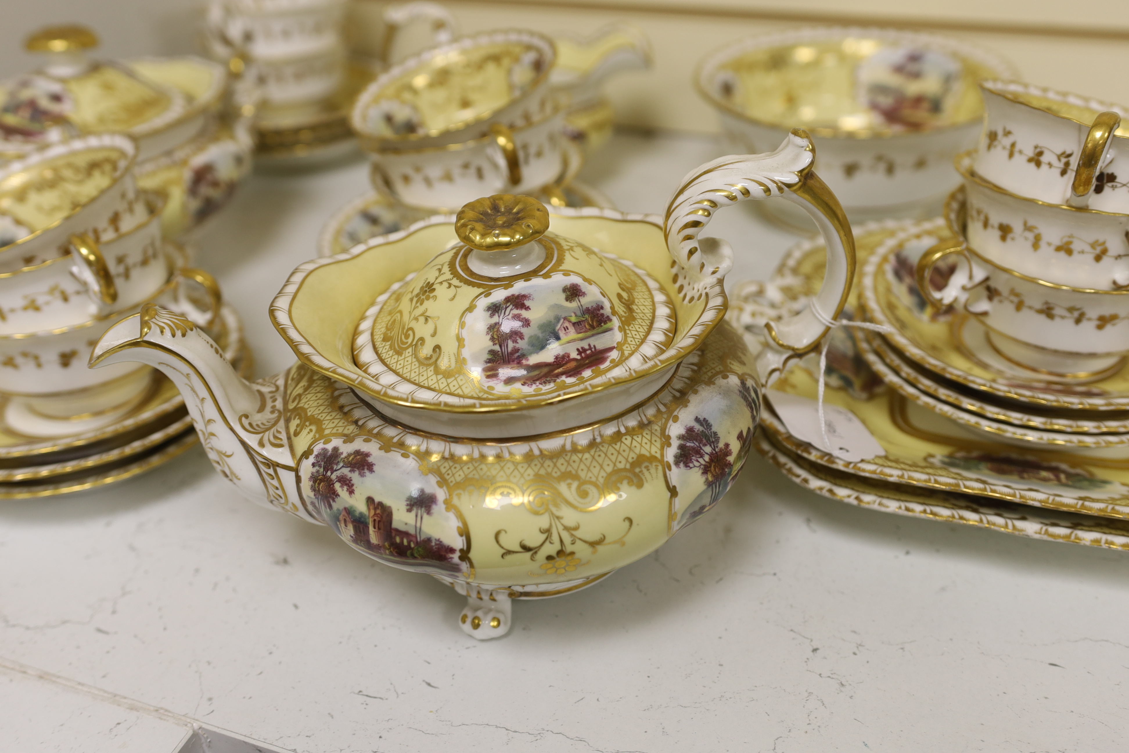 An English porcelain tea set, c.1835-45, including a teapot and cover, sucrier and cover, slops bowl, milk jug, teacups and saucers, two cake plates, each piece painted with buildings in landscapes, yellow ground, patter